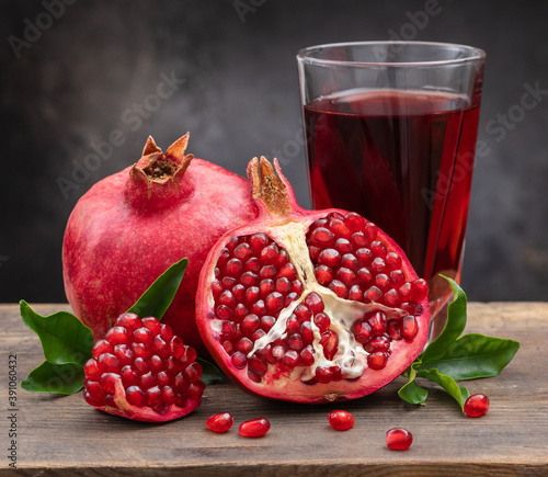 Obraz na plátne Ripe pomegranate, half a juicy pomegranate and healthy pomegranate juice in a glass on a cutting board, side view, dark vintage background