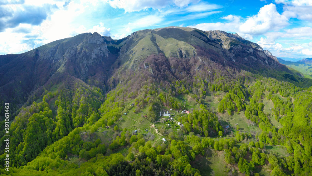 Aerial drone view of Buila Vanturarita Massif and Patrunsa Monastery - a rural settlement located on the hills at the base of the mountain.
