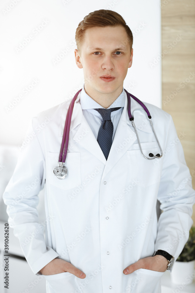 Man-doctor standing straight in sunny clinic. Medicine concept Man-doctor standing straight in sunny clinic. Medicine concept