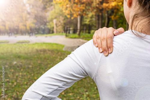 Young woman hand holding shoulder, back pain. Nature, park, sunny weather