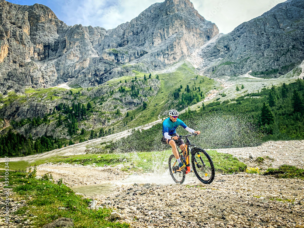 Fototapeta premium Man doing mountain biking in a mountain route - Sport Man riding a mountain bike passes in through a shallow stream running through tranquil nature