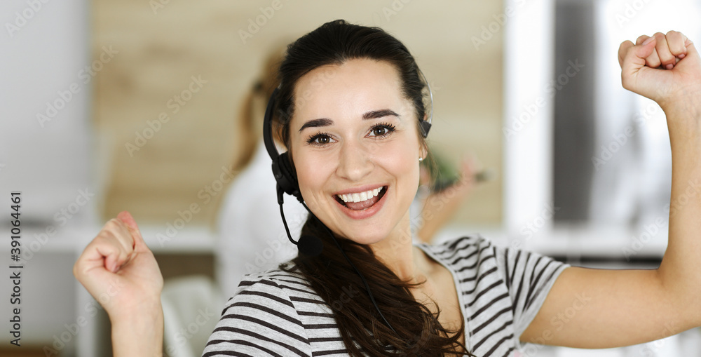 Business woman using headset for communication and consulting people at customer service office. Call center. Group of operators at work at the background. Casual dress style