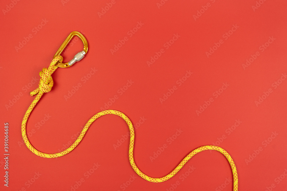 Overhand knot with orange carabiner and yellow climbing rope on red background Overhand knot with orange carabiner and yellow climbing rope on red background