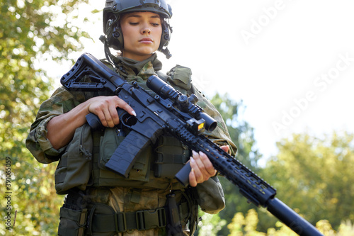 young caucasian military woman is checking rifle in the forest before shooting, alone in nature, female soldier