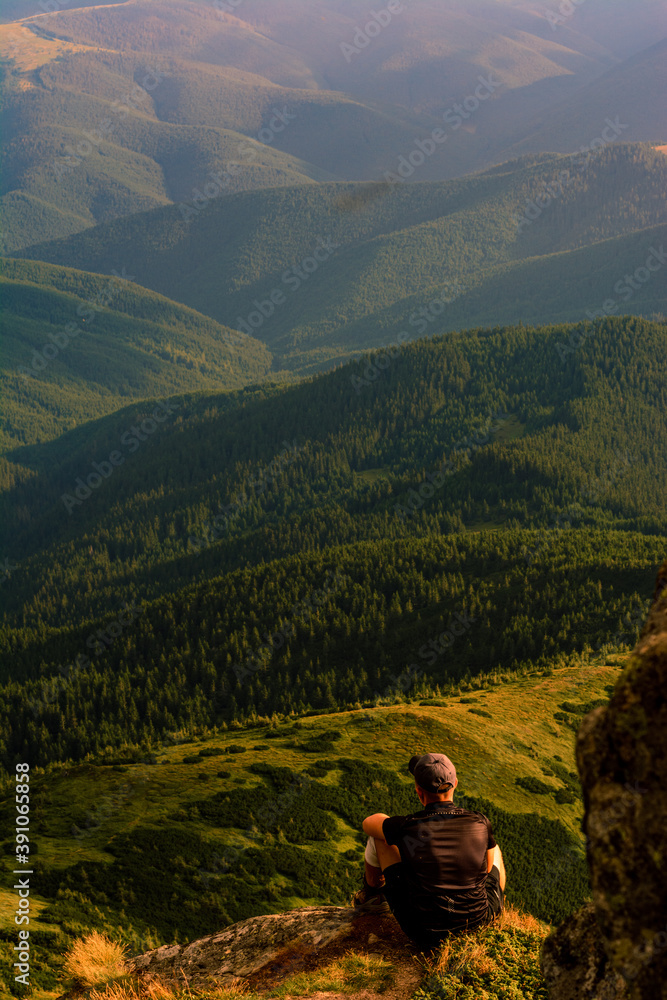 Naklejka premium A tourist sits on a rock and looks into the distance, photos on top of Mount Pip Ivan Chornohirsky, landscapes and epic photos of tourists in the mountains.