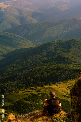 A tourist sits on a rock and looks into the distance, photos on top of Mount Pip Ivan Chornohirsky, landscapes and epic photos of tourists in the mountains.