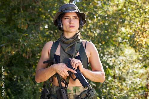 Fototapeta Naklejka Na Ścianę i Meble -  powerful sportive woman soldier ready for battle wearing protective military gear weapon, rifle or gun. in wild nature