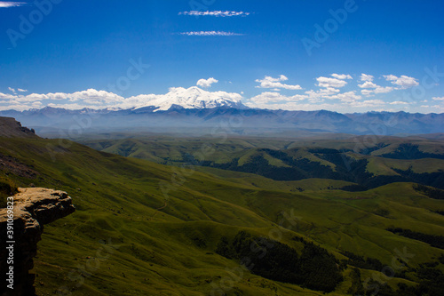 An excellent view from the plateau to the extinct volcano and the snowy peak of Mount Elbrus. Below is a green gorge