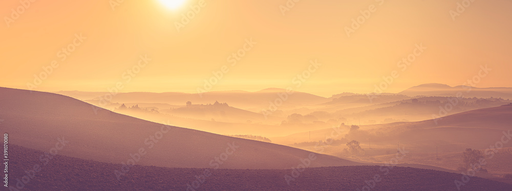 Morning golden hour panorama of Tuscany landscape with mist, rolling hills and farm houses