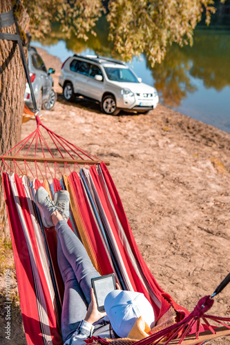 woman reading book laying on hammock outdoors at river beach