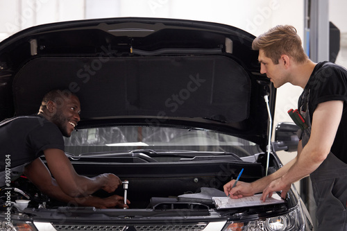 two auto mechnic colleagues discuss what to do, repait cat hood together, have conversation photo