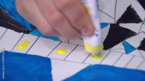 A cute girl draws a multicolored ornament on paper with acrylic paints and a brush.