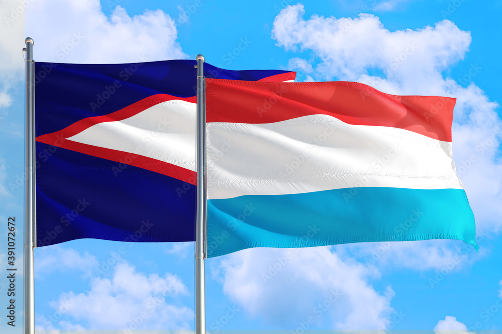 Luxembourg and American Samoa national flag waving in the windy deep blue sky. Diplomacy and international relations concept. Luxembourg and American Samoa national flag waving in the windy deep blue sky. Diplomacy and international relations concept.