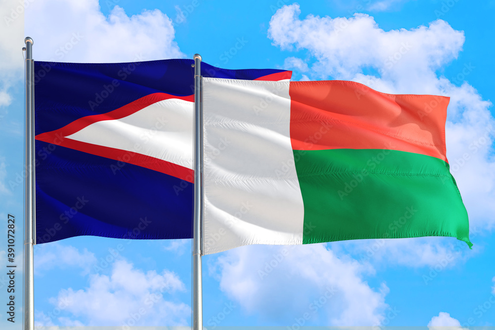 Madagascar and American Samoa national flag waving in the windy deep blue sky. Diplomacy and international relations concept. Madagascar and American Samoa national flag waving in the windy deep blue sky. Diplomacy and international relations concept.
