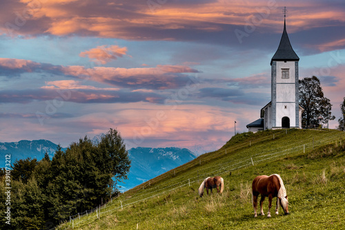 Horse Grazing at Picturesque  Church Of St Primoz.in Jamnik,Kamnik, Slovenia at Sunset with Beautiful Sky photo