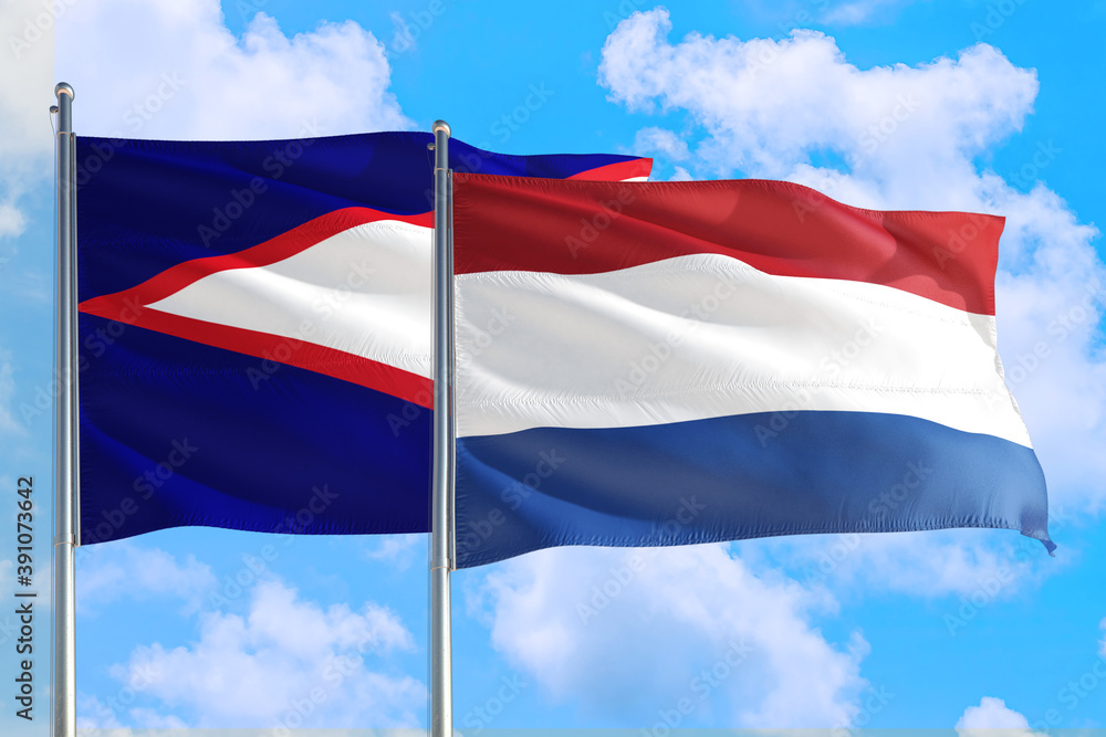 Netherlands and American Samoa national flag waving in the windy deep blue sky. Diplomacy and international relations concept. Netherlands and American Samoa national flag waving in the windy deep blue sky. Diplomacy and international relations concept.