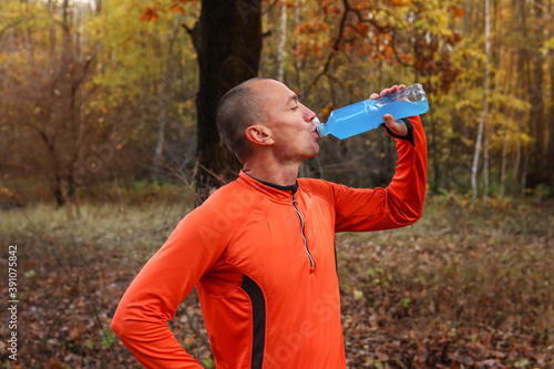 Male runner, athlete, drinks isotonic, energy drink after a hard workout in the open air. Sports nutrition