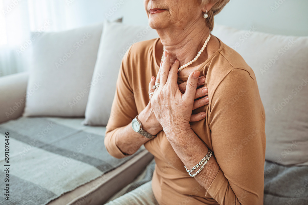 Senior Woman Suffering From Chest Pain While Sitting on Sofa at Home. Portrait of Elderly Woman Having Heart Attack. Heart problems can affect anyone at any time Senior Woman Suffering From Chest Pain While Sitting on Sofa at Home. Portrait of Elderly Woman Having Heart Attack. Heart problems can affect anyone at any time