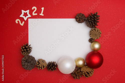 Christmas layout on a red background. New Year card with white sheet for text, with numbers 2021, Christmas balls, fir cones on a red background. The basis for a festive New Year's layout. Copyspace