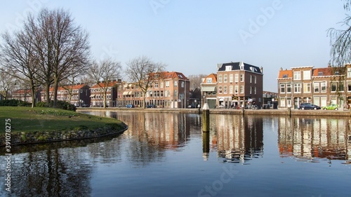 View on channel and street in Delft in Neherlands. Buildings reflected in the water. trees, bicycles, boats in the frame. Photo taken during sunny spring day.