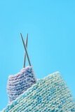 knitted scarf with knitting needles on a blue background.
