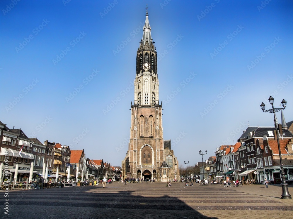 The Nieuwe Kerk - New Church. Protestant church in the city of Delft in the Holland. The building is located on Delft Market Square - Markt. Cloudless blue sky and people walking around.
