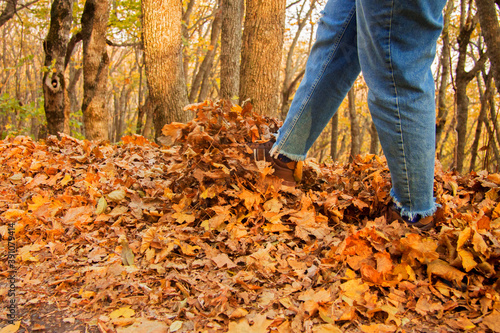 Womans leg kicks yellow autumn leaves from the ground in the park