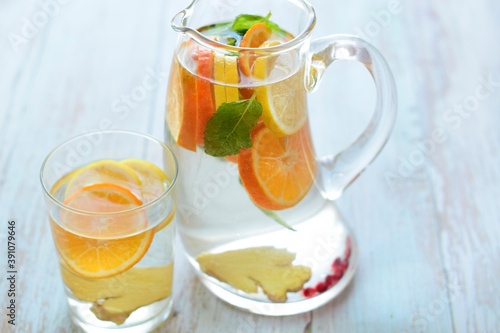 water in a teapot and a glass with lemon wedges, tangerine, mint leaves, ginger root