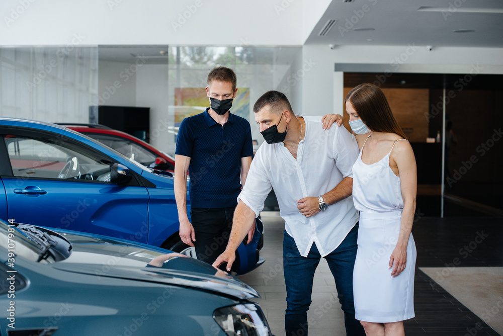 Young couple in masks selects a new vehicle and consult with a representative of the dealership in the period of the pandemic. Car sales, and life during the pandemic Young couple in masks selects a new vehicle and consult with a representative of the dealership in the period of the pandemic. Car sales, and life during the pandemic