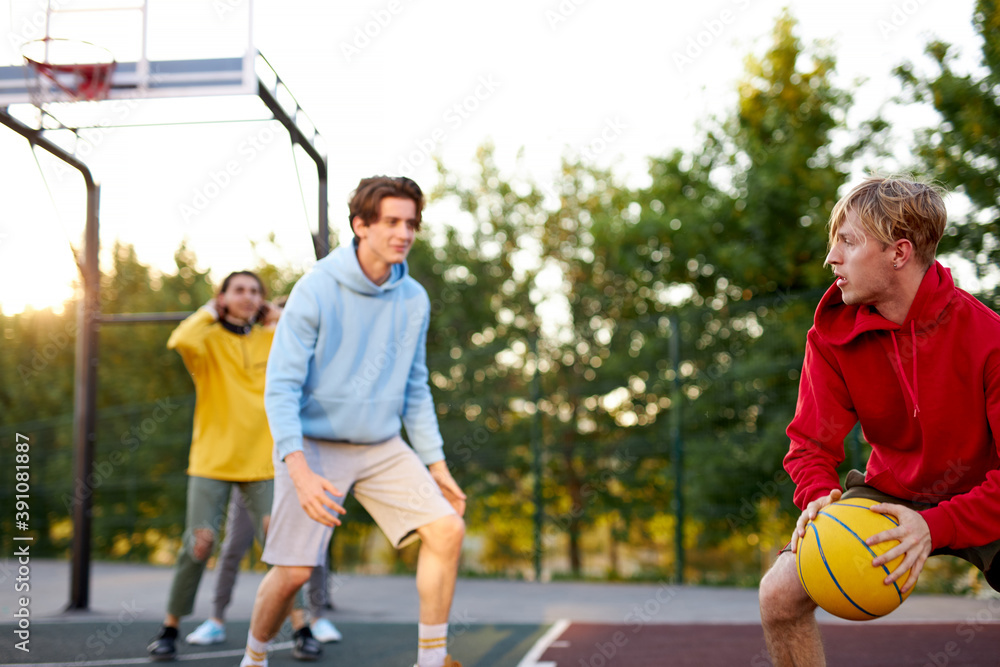 teens boys playing basketball on outdoor court, playground and having fun, caucasian young guys dribbling basketball with friends blocking