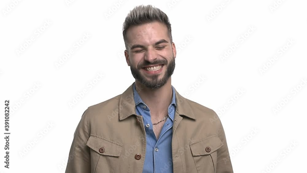 happy young man in denim shirt having fun and laughing, adjusting beige jacket and crossing arms, standing isolated on white background in studio