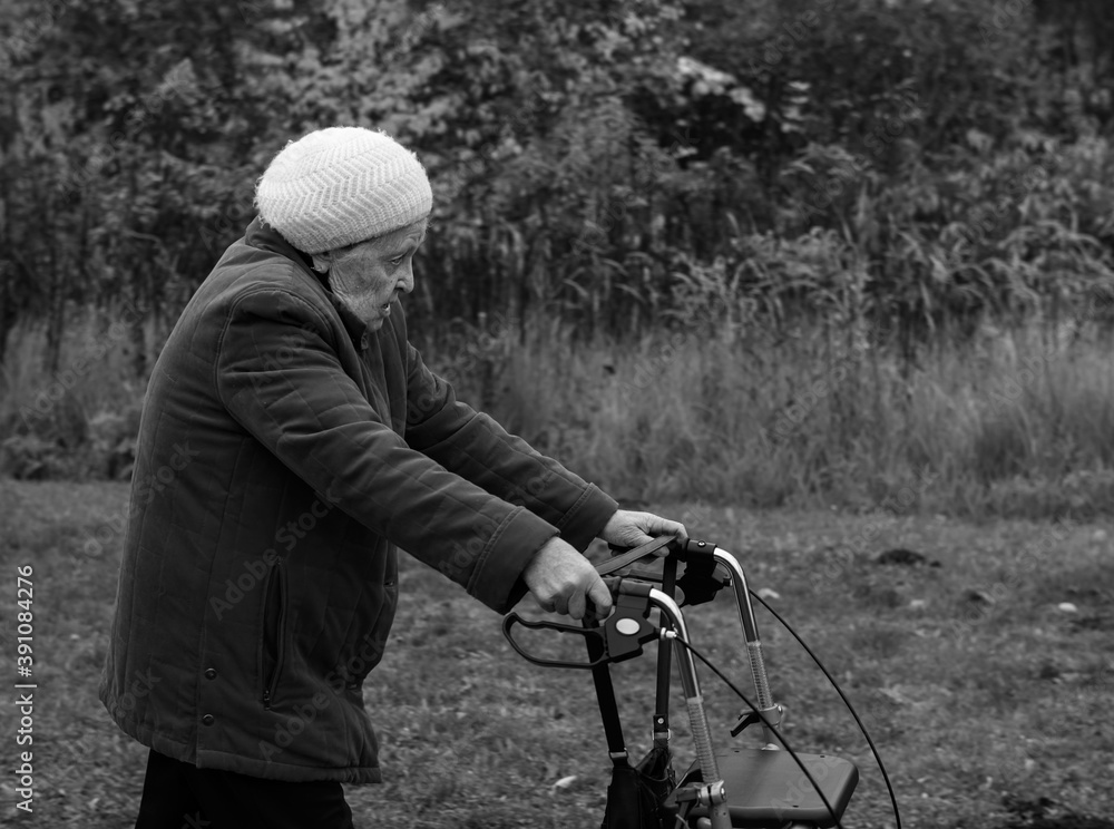 Elderly woman taking a walk in winter with the help of a walker aid in black and white