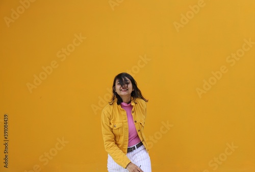 A very happy brown southeast Asian wearing yellow jacket and white pants laughing in front of a clear yellow wall 