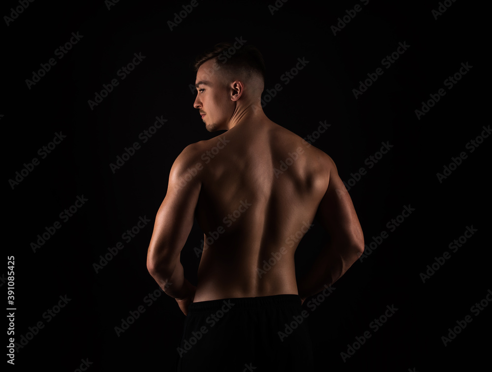 Handsome young bodybuilder with muscular back standing on black background Handsome young bodybuilder with muscular back standing on black background
