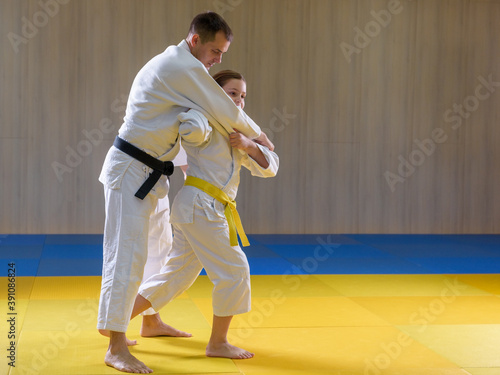 Young female yellow belt judoka setting up older black belt male judoka for throw
