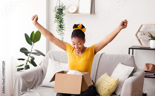 Excited black lady unboxing parcel after online shopping