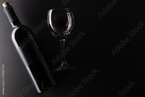 Elegant bottle and wineglass of red wine on black background. Top view. Flat lay. Concept of advertising and promotion of alcoholic drinks. Space for text.