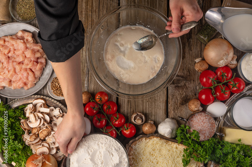 Chef hands makes dough on wooden rustic table with variety of ingredients background. Concept of cooking process. Backstage of preparing tasty meal. View from above. Flat lay.
