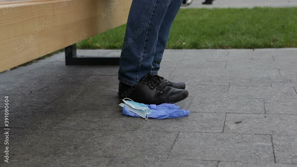A man sitting on a bench in a city park threw a used medical mask and gloves on the ground. A man sitting on a bench in a city park threw a used medical mask and gloves on the ground.