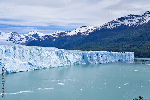 Blue ice of Perito Moreno Glacier in Glaciers national park in Patagonia, Argentina with turquoise water of Lago Argentino in the foreground, dark green forests and sow covered mountains of the Andes