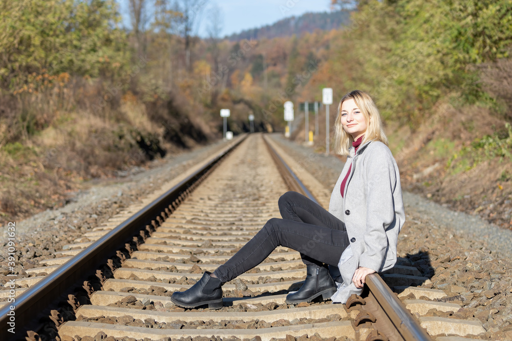 Young woman is sitting on the rails and looking at the camera in the sunny autumn day