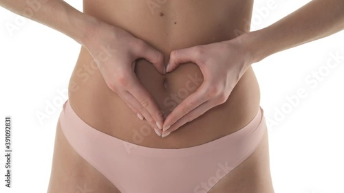Front view of flat Caucasian woman's belly. Unrecognizable model showing heart shape sign across her stomach. Isolated on white background