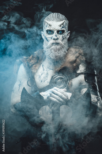 Nordic savage undead in dark armour with white skin and blue eyes holding his huge axe in smokey and dark background.