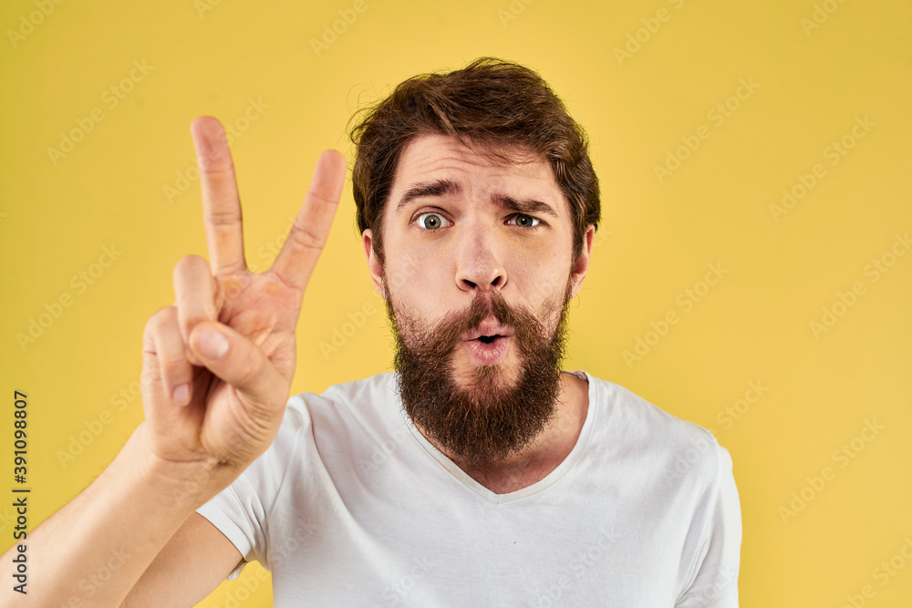 Bearded man emotions fun gesture with hands white t-shirt close-up yellow background Bearded man emotions fun gesture with hands white t-shirt close-up yellow background