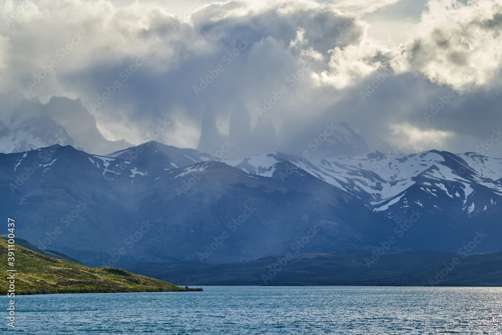 Towers of torres del Paine national park covered in clouds with dark green forest a lake and snow covered mountains of the Andes in Patagonia southern Chile