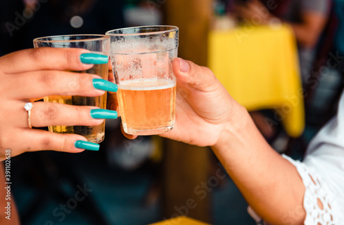 Two girl friends toasting with glasses of light beer on typical brazilian cup (americano long drink).
