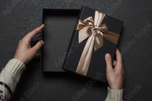 Open gift box with golden ribbon and bow. The guy opens a black gift box