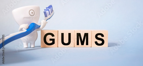 The inscription GUMS on wooden cubes on a light blue background together with pedmets related to stomatology. Health and medicine concept.