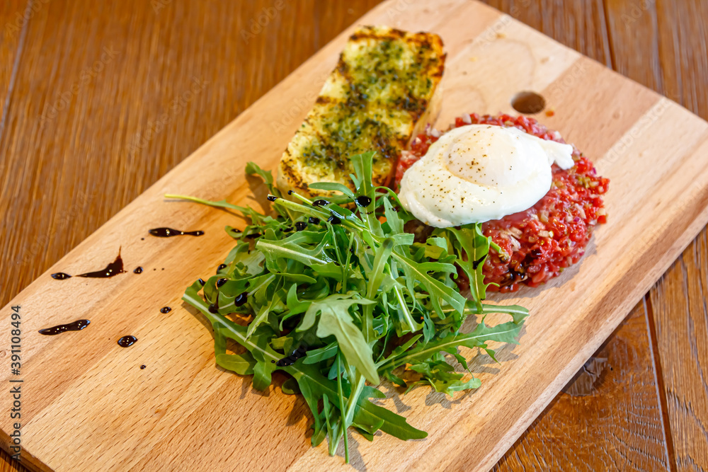 Raw beef tartare with arugula and poached egg on a wooden Board Raw beef tartare with arugula and poached egg on a wooden Board