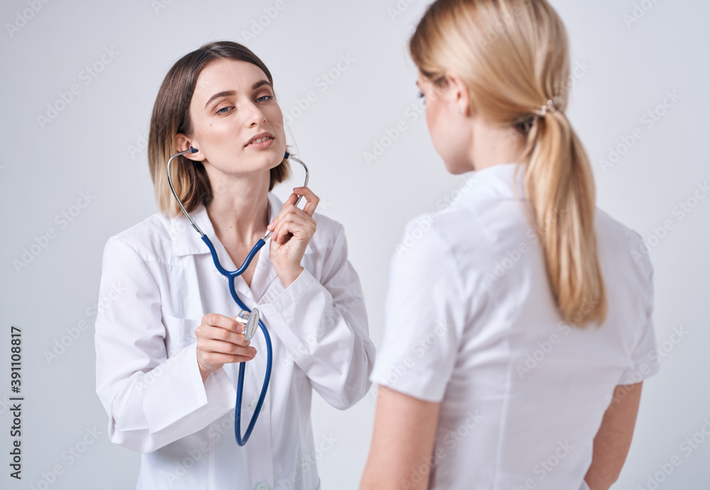 doctor with a stethoscope examines a woman in a white t-shirt on a light background doctor with a stethoscope examines a woman in a white t-shirt on a light background